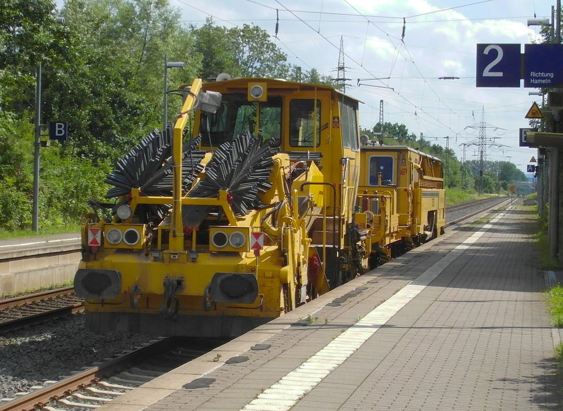 Schotterplaniermaschine im Gleisbereich an einem Bahnsteig bei Tageslicht
