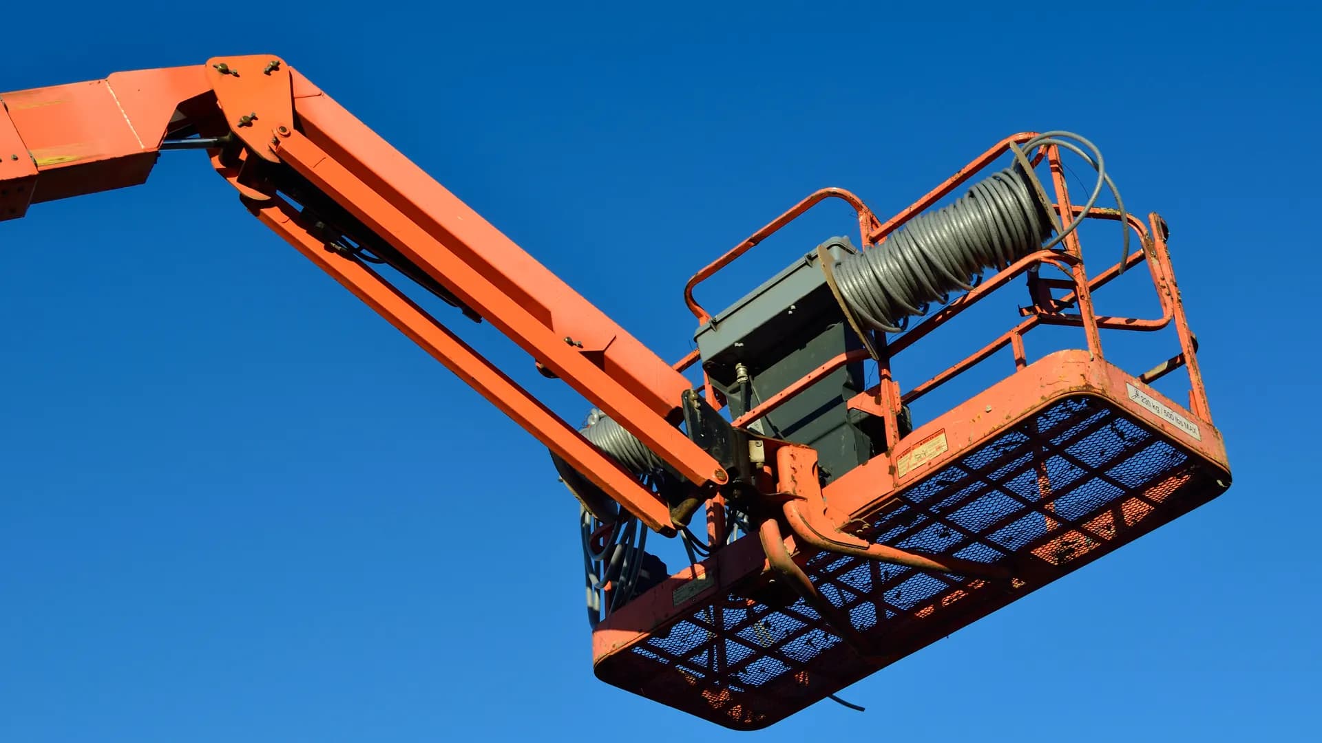 Arbeitskorb am Gelenkausleger einer Hubarbeitsbühne, von unten gegen den Himmel aufgenommen